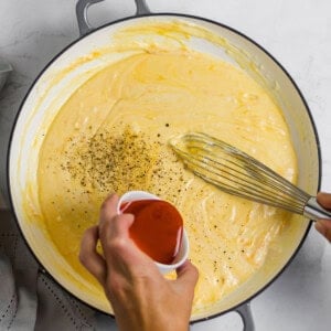 adding hot sauce to mac and cheese sauce.