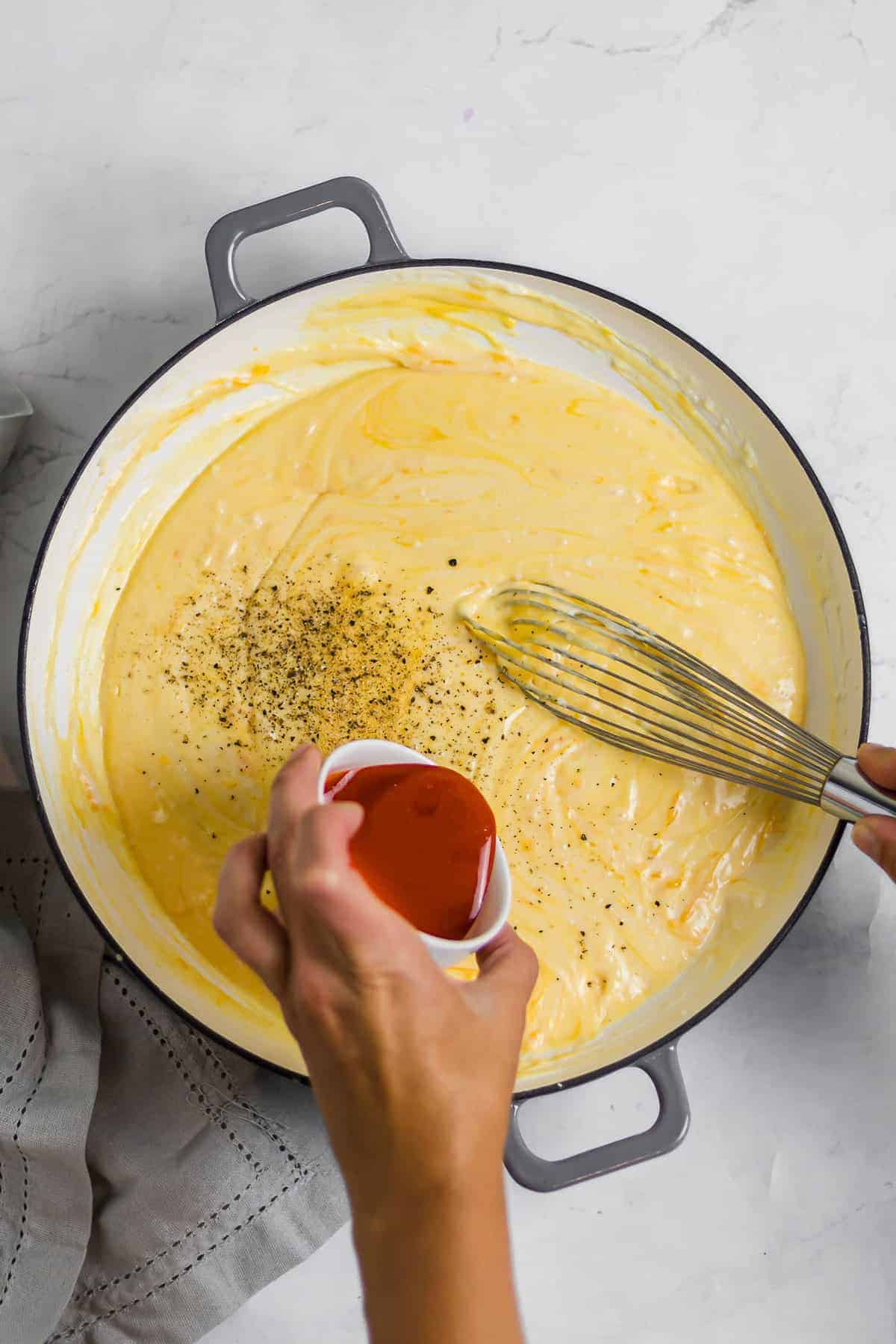 hot sauce being added to mac and cheese sauce and whisked together.