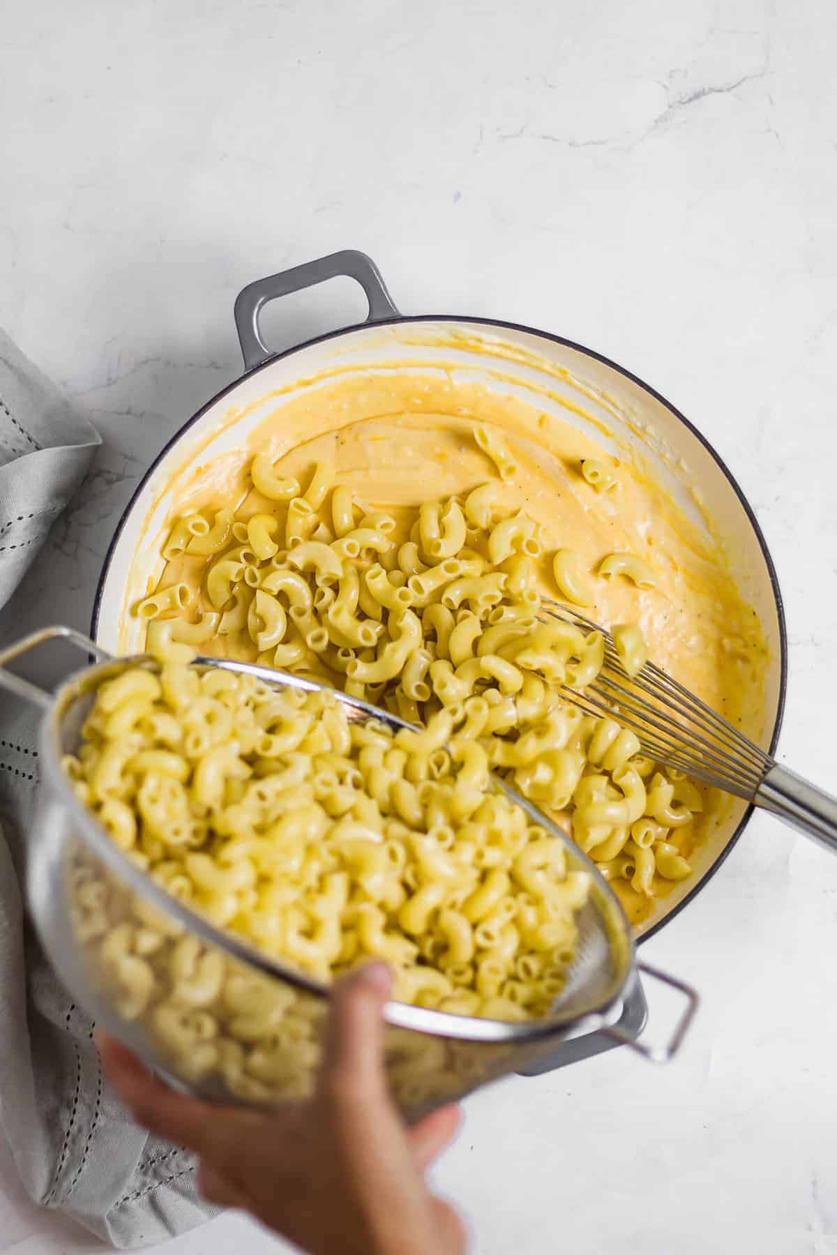 macaroni noodles being added to mac and cheese sauce and stirred together.