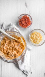 a bowl full of ingredients for a Mexican dip featuring Buffalo chicken nachos.