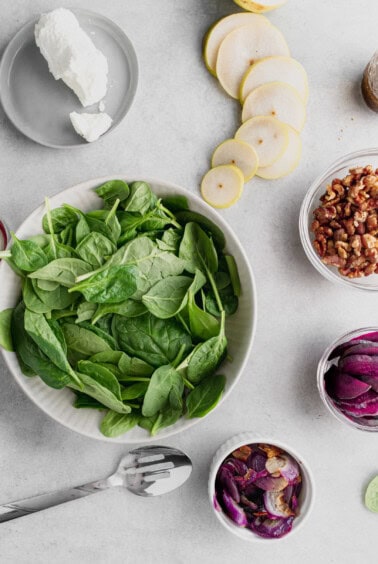 ingredients for a beet and goat cheese salad with spinach and red onion.