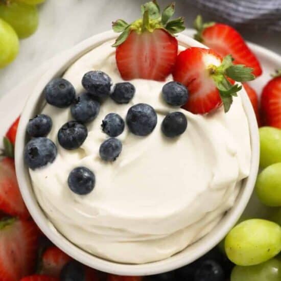 close up image of cream cheese fruit dip in a bowl surrounded by fresh fruit