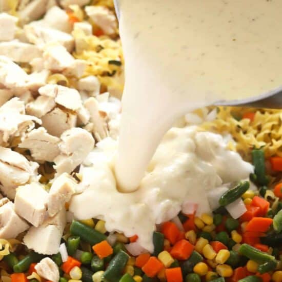 Creamy sauce poured over chicken and vegetables in a casserole dish for the perfect creamy chicken noodle casserole.