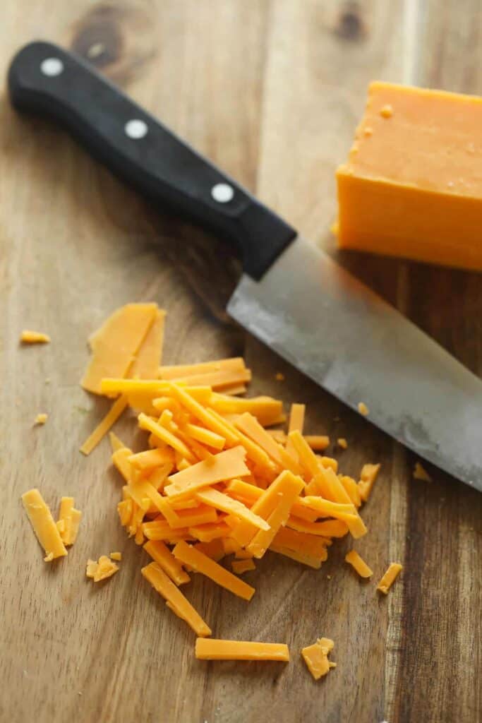 Shredded cheese on a cutting board by a knife.
