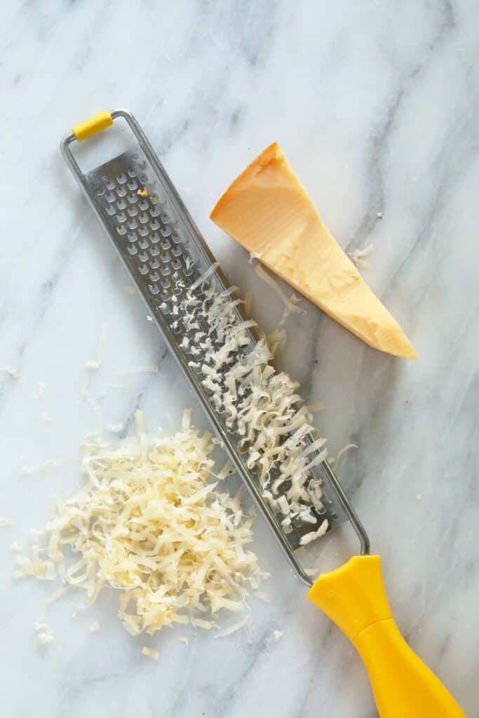 A zester and a piece of cheese on a cutting board. 