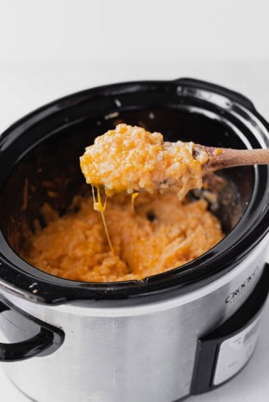 A wooden spoon stirs a crockpot of cheesy macaroni and cheese.