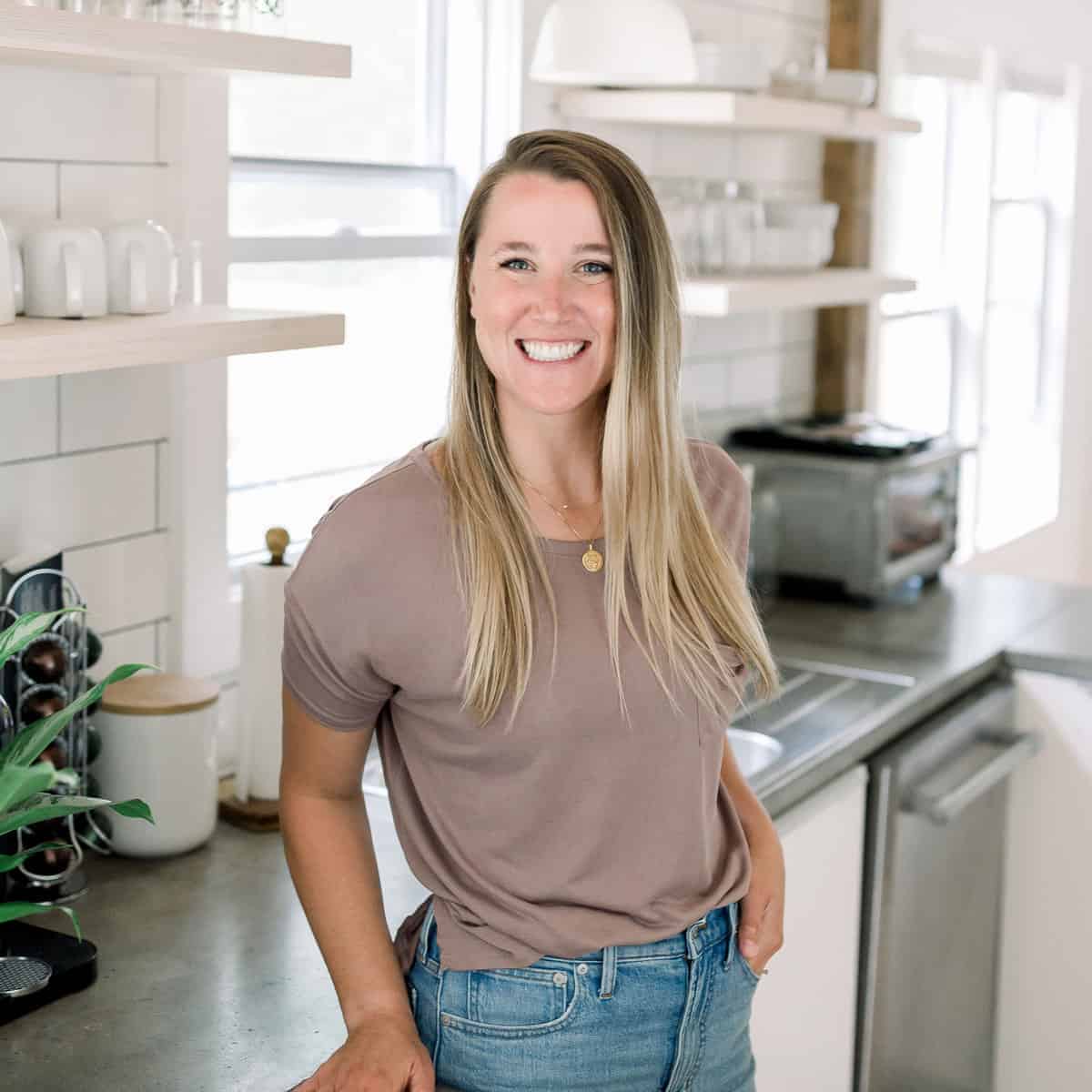 a woman in jeans and a t - shirt standing in a kitchen.