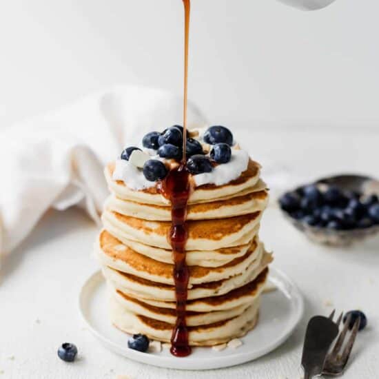 A stack of ricotta pancakes with blueberries being drizzled with syrup.