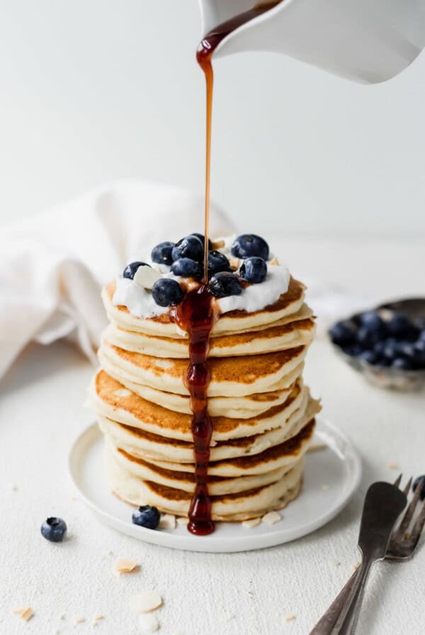 A stack of ricotta pancakes with blueberries being drizzled with syrup.