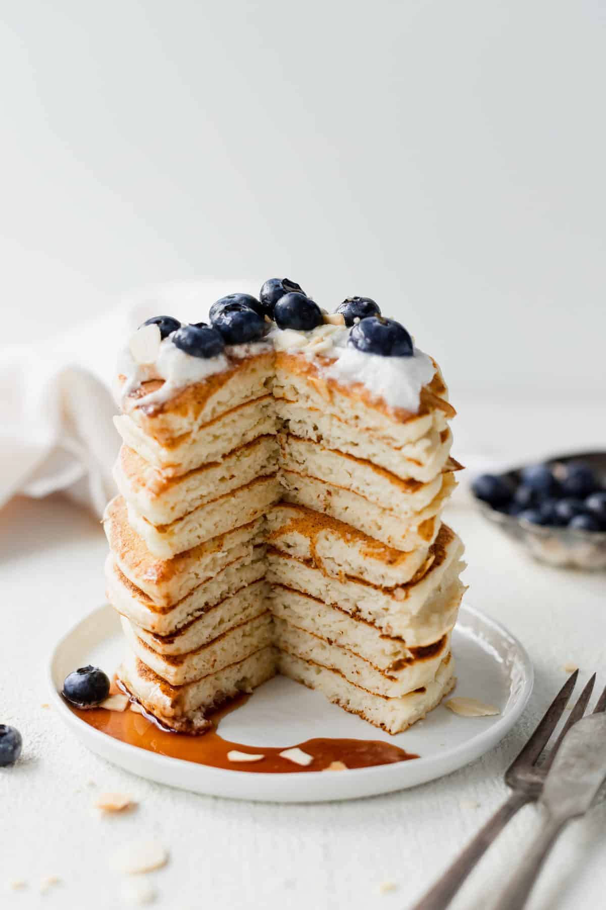 Stack of ricotta pancakes on a plate and topped with blueberries.