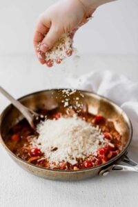 A person sprinkling parmesan on sun dried tomato pasta.