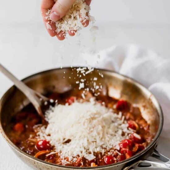 A person sprinkling parmesan on sun dried tomato pasta.