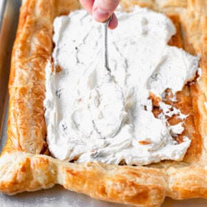 a person spreading cream on a tomato tart.