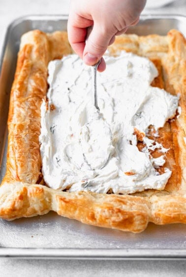 a person spreading cream on a tomato tart.