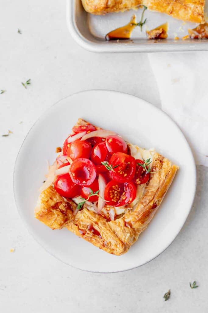 slice of tomato tart on a plate topped with fresh thyme.