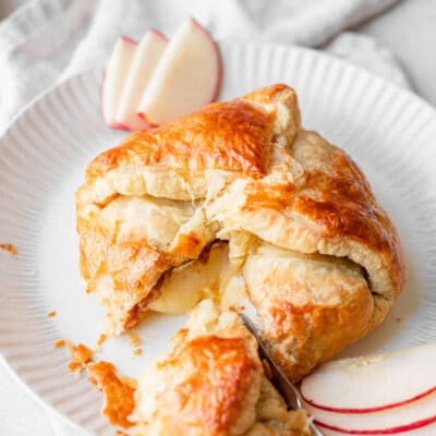 Baked Brie wrapped in golden puff pastry, cut open on a white plate with apple slices.