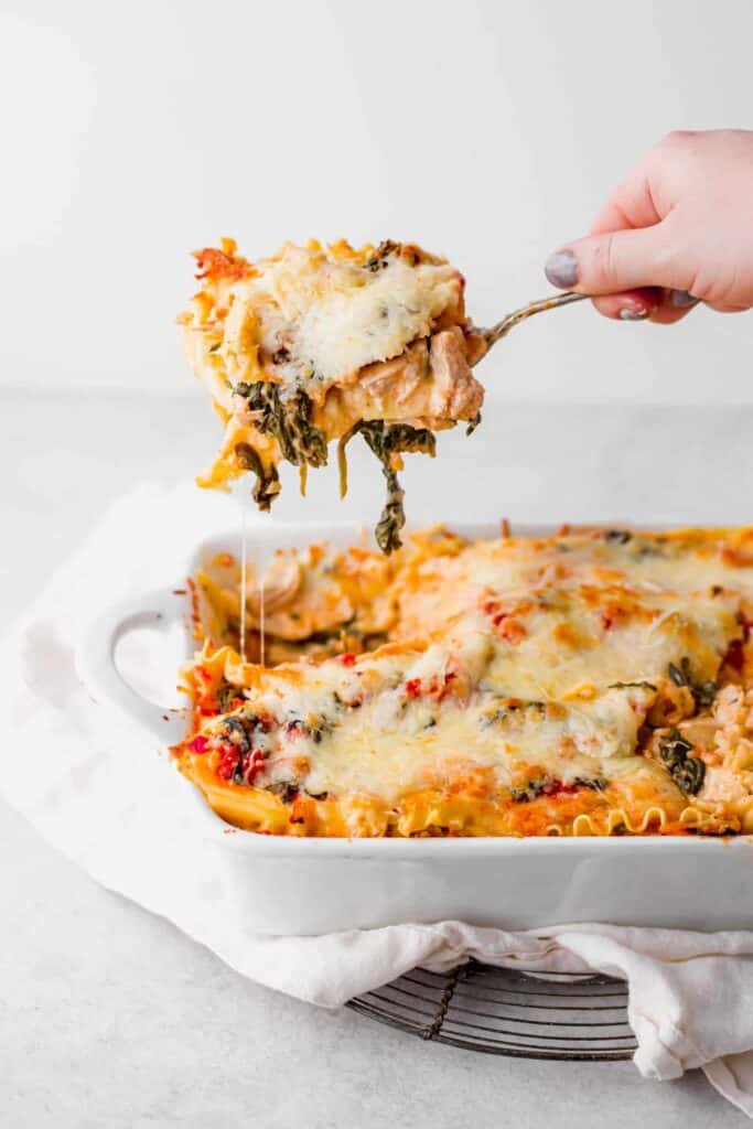 A piece of lasagna being lifted up out of a casserole dish. 