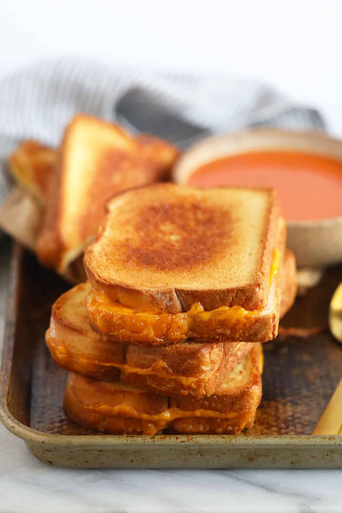 sheet pan grilled cheese sandwiches next to a bowl of tomato soup