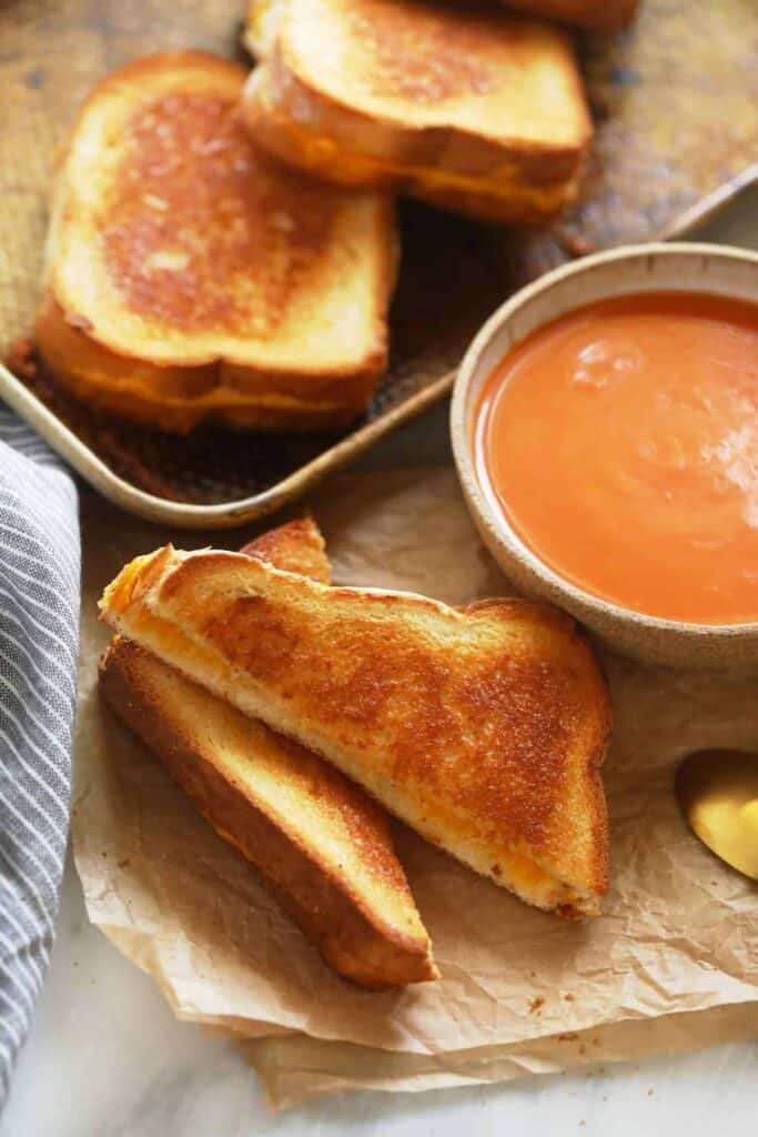 sheet pan grilled cheese sandwiches next to a bowl of tomato soup