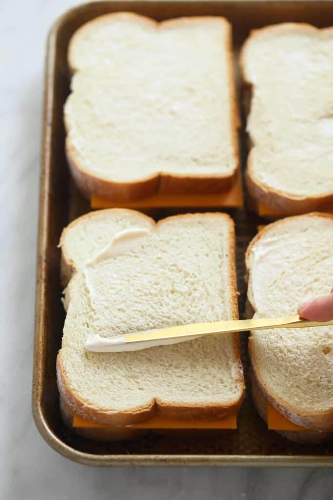 sheet pan grilled cheese sandwiches being spread with butter on the outside of the bread