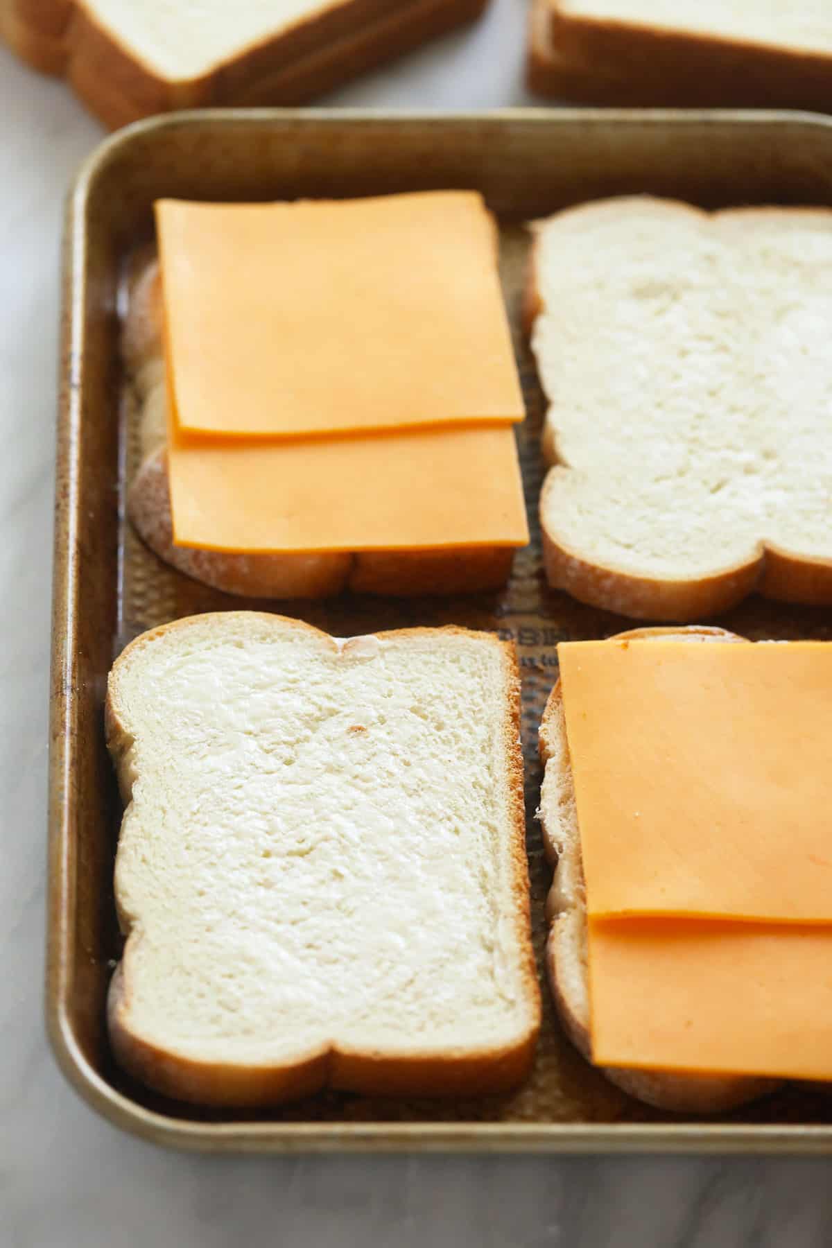 sheet pan grilled cheese sandwiches being assembled on a sheet pan before being baked