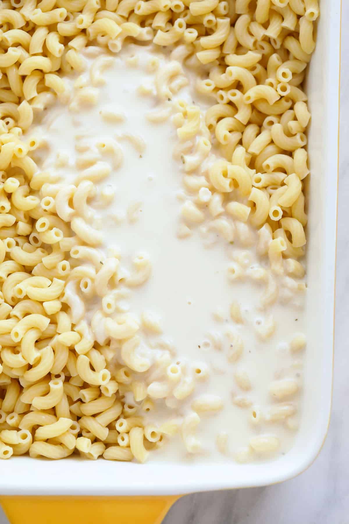 cheese sauce poured over baked mac and cheese in a casserole dish