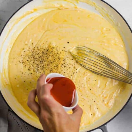 buffalo sauce being poured into mac and cheese sauce