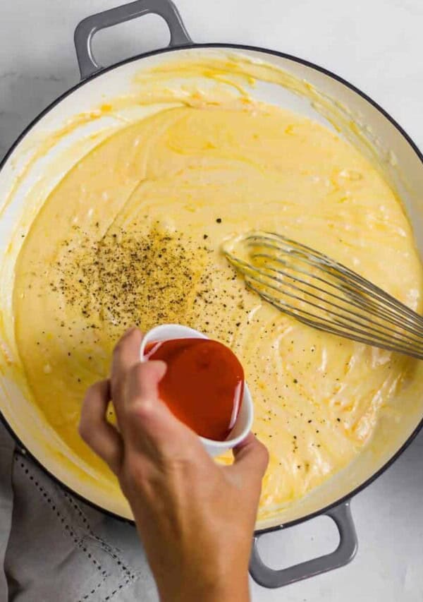buffalo sauce being poured into mac and cheese sauce