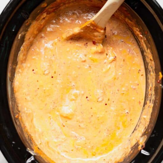 A slow cooker queso dip served in a bowl with a wooden spoon.