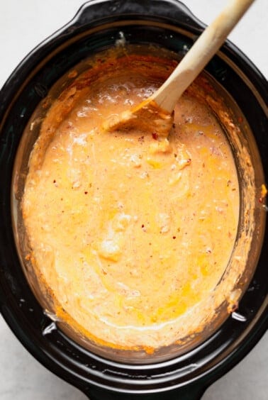 A slow cooker queso dip served in a bowl with a wooden spoon.