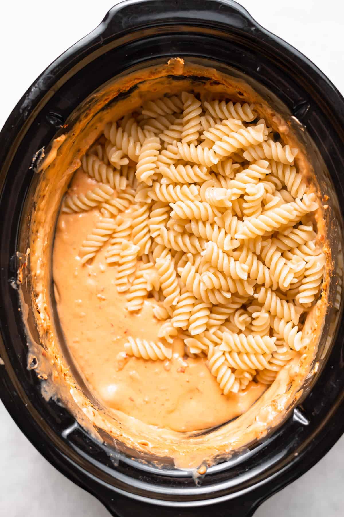 Noodles and queso dip in a slow cooker. 