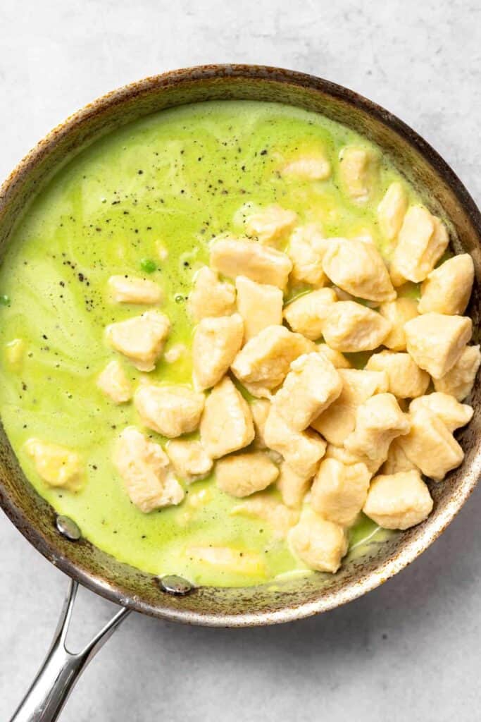 blended sweet pea butter sauce with cooked gnocchi in a skillet, ready to be mixed together
