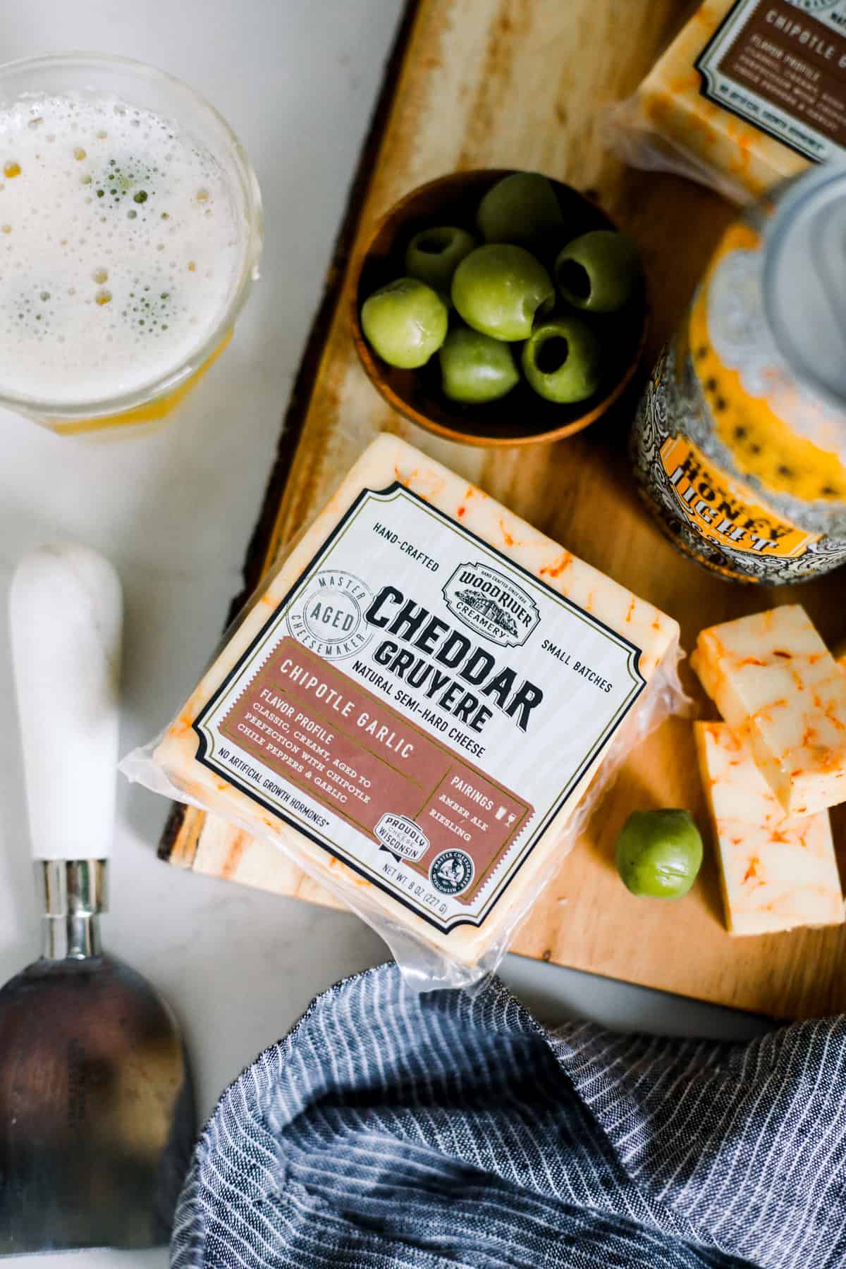 chipotle garlic cheese with green olives and a honey light lager on a cutting board