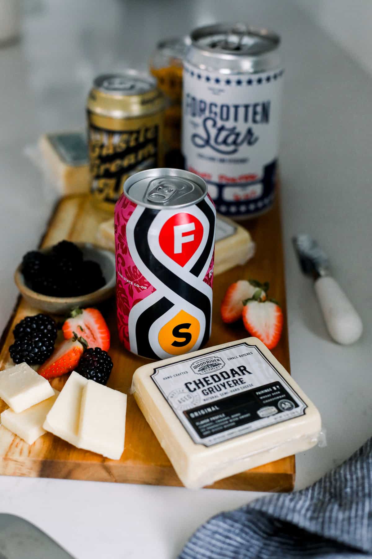 beer and sliced cheese with sliced fruit on a cutting board