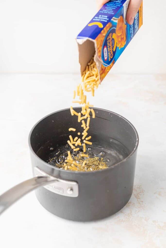 Pouring boxed mac and cheese into a saucepan.