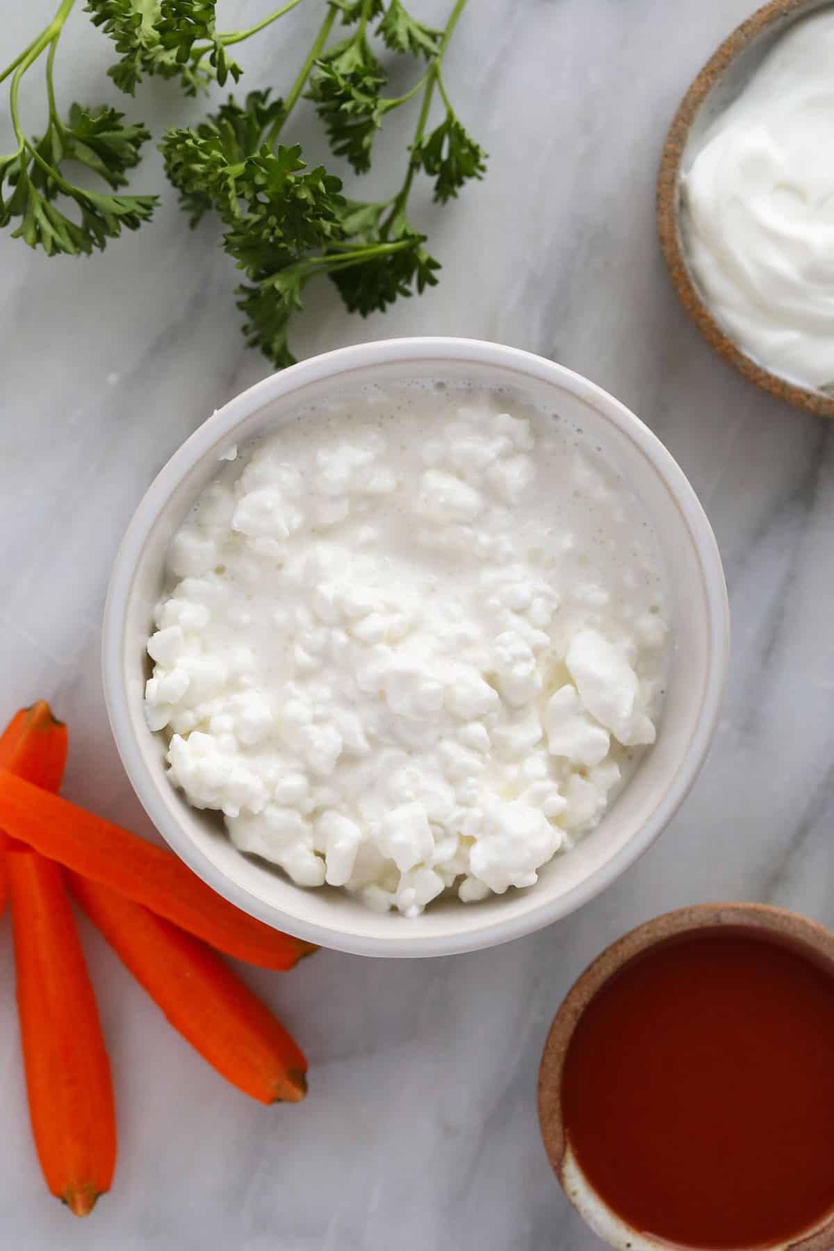 cottage cheese, greek yogurt and buffalo sauce in bowls ready to be whipped in a food processor