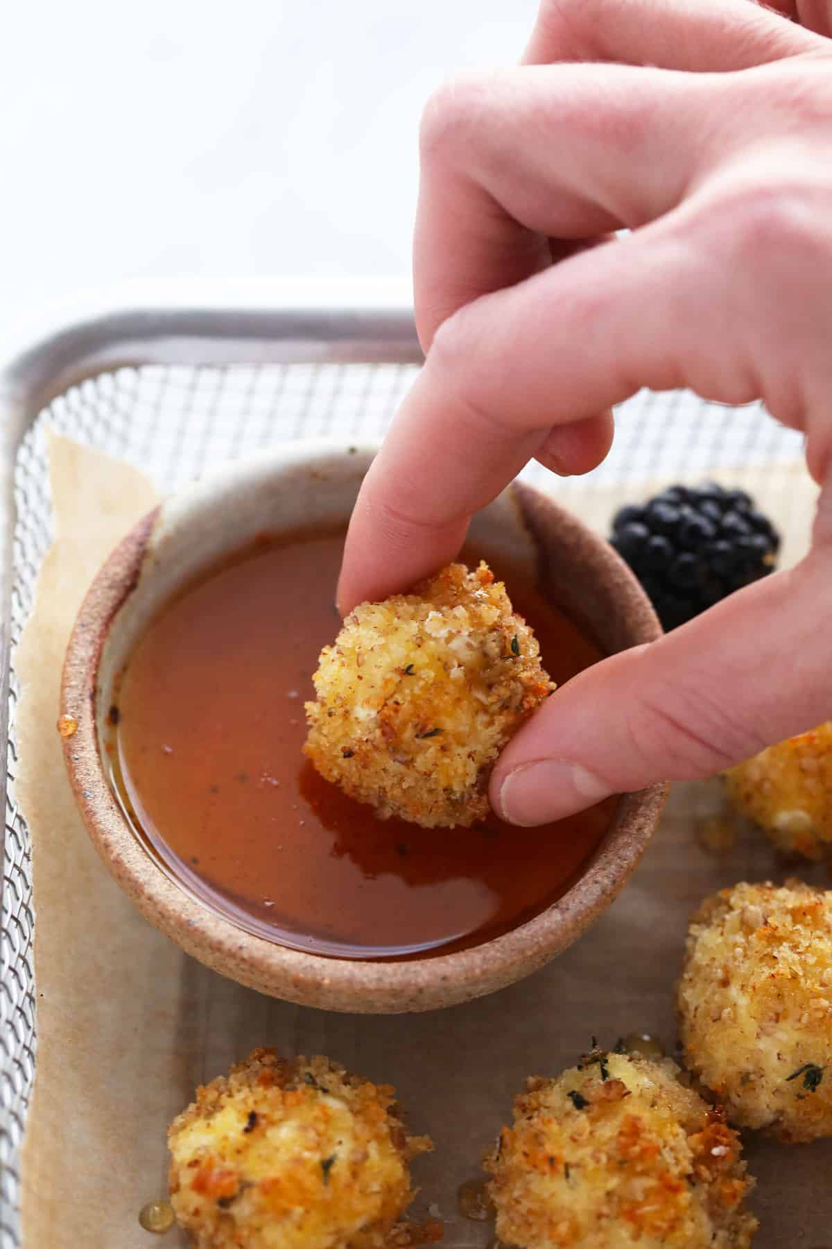 dipping goat cheese ball in honey sriracha sauce