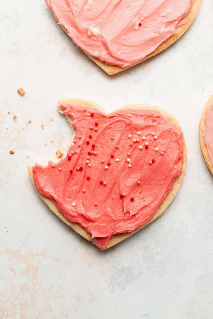 cream cheese heart cookie frosted with pink frosting and sprinkles, and a bite taken out of it
