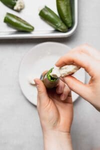 a person putting cream cheese on a jalapeno pepper.