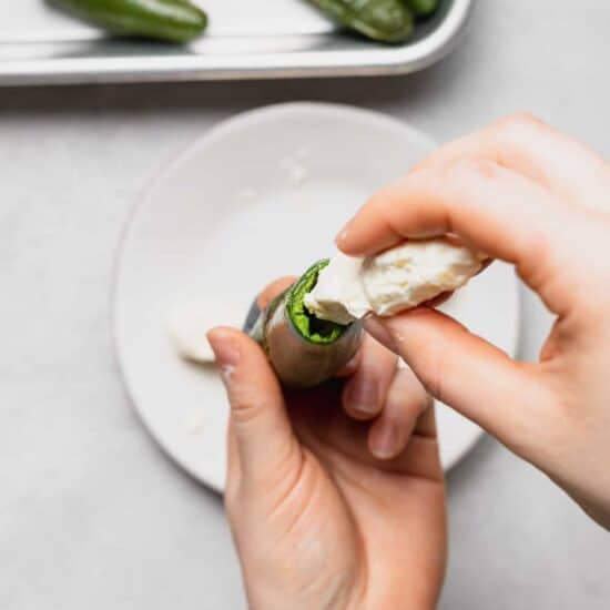 a person putting cream cheese on a jalapeno pepper.