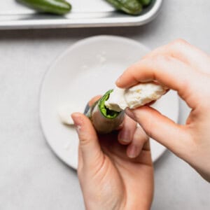 a person putting cream cheese on a jalapeno pepper.