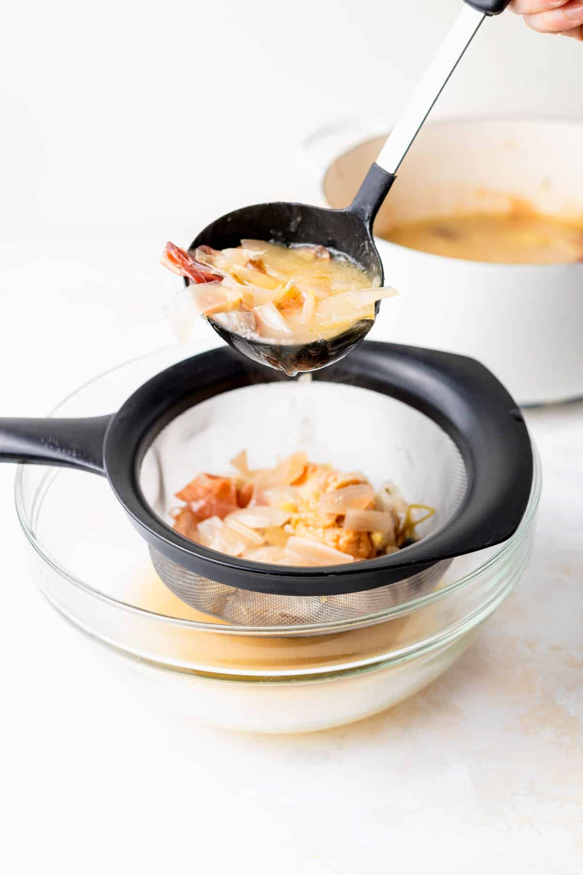 parmesan broth being strained through a sieve to remove the ingredient chunks