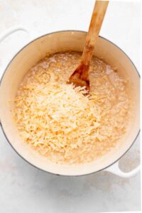 a pot of rice with cheese and a wooden spoon.