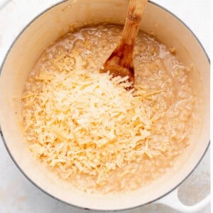 a pot of rice with cheese and a wooden spoon.