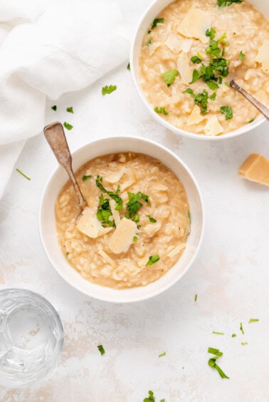two bowls of risotto with parmesan cheese and parsley.