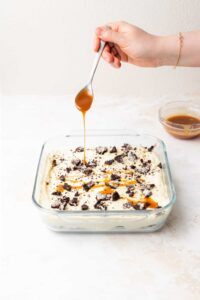 a person is drizzling caramel sauce over a dessert in a baking dish.