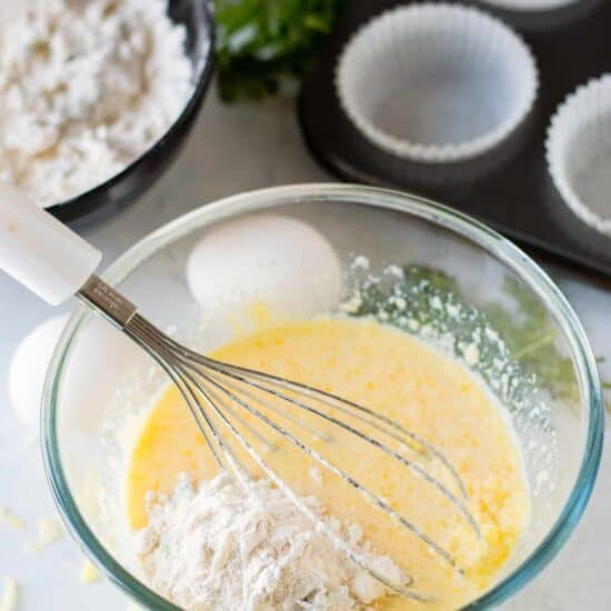 A bowl with eggs, flour, and a whisk used to make cheese muffins.