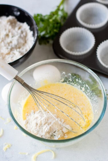A bowl with eggs, flour, and a whisk used to make cheese muffins.