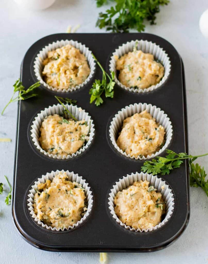 savory cheese muffin batter in muffin liners in a muffin tin, ready to be placed into the oven and baked