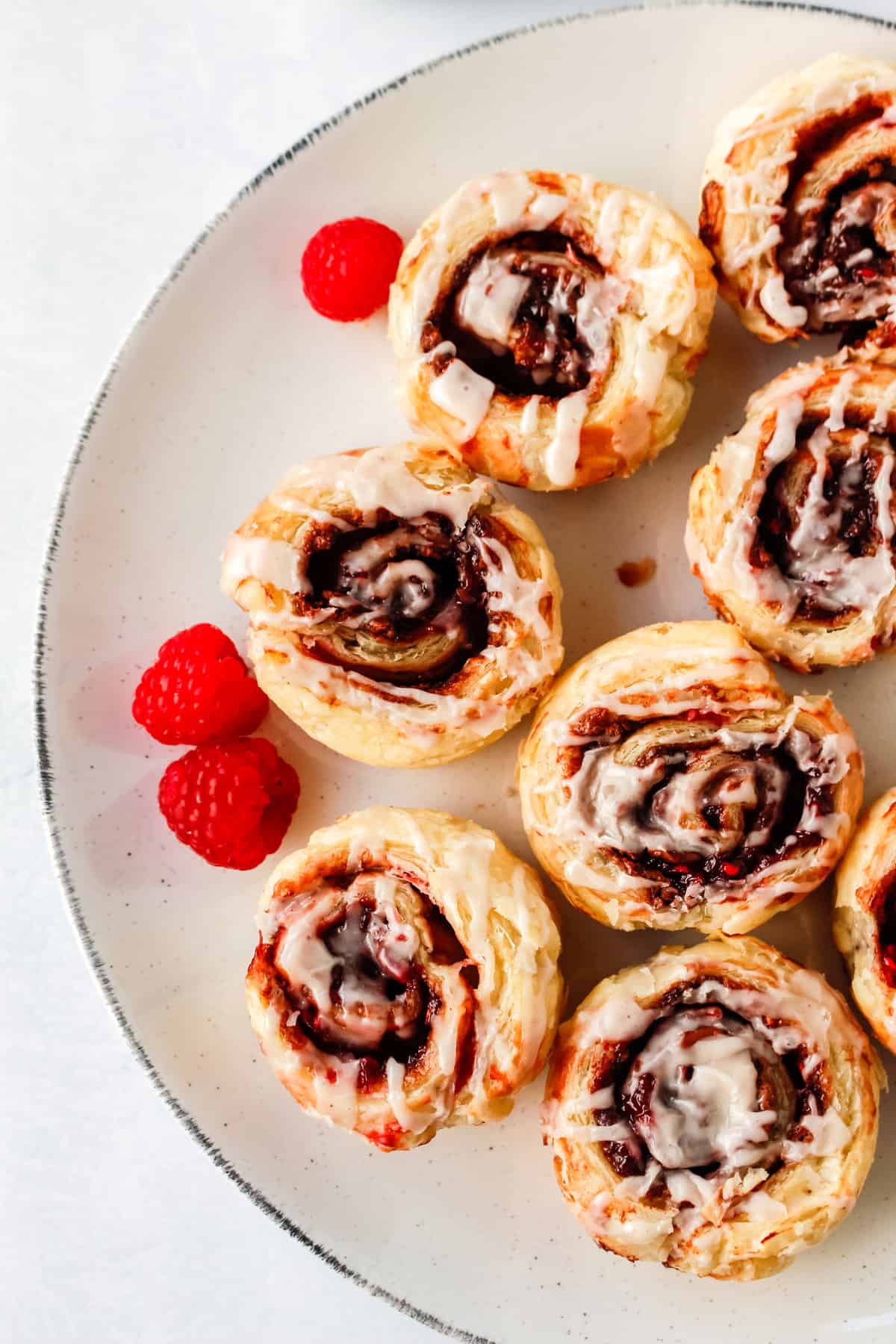 chocolate raspberry cinnamon rolls on a plate surrounded by fresh raspberries